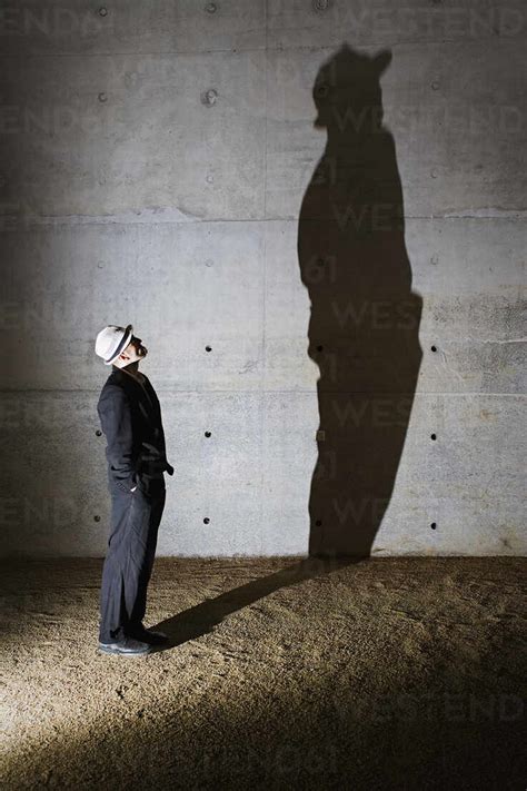 Man Looking Up At Tall Shadow On Wall Stock Photo
