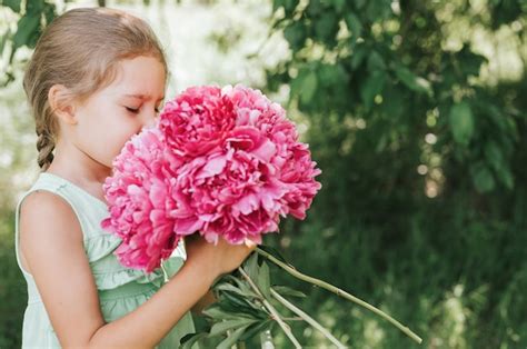 Szczęśliwa Mała Dziewczynka Trzyma W Rękach Bukiet Różowych Kwiatów Piwonii W Rozkwicie