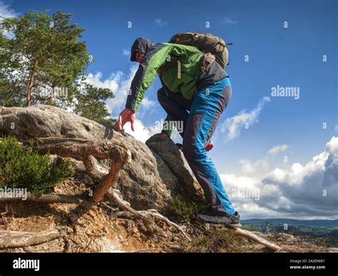 Man Climbing Steep Mountain Slope Sunny Windy Day In Rocks Stock Photo