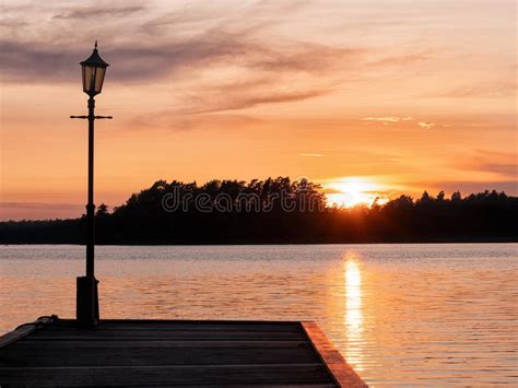 Picture Of Lakeside Sunset With Wooden Pier And Trees At The Background