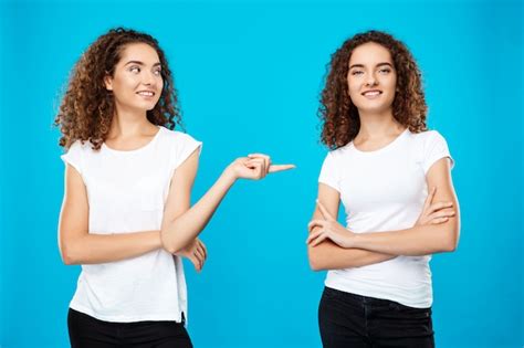 Free Photo Girl Pointing Finger At Her Sister Twin Over Blue Wall