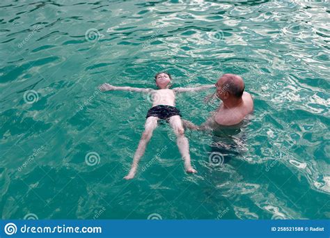 Grandfather Teaches His Grandson To Swim On His Back In Pool Stock