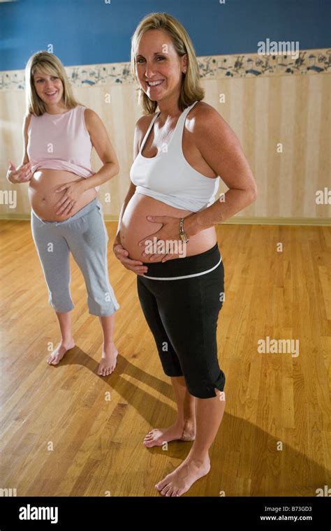 Two Pregnant Women Together In Exercise Studio Tummy Showing Stock