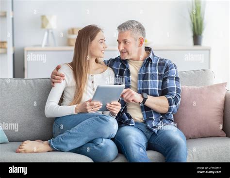 happy mature couple with tablet pc sitting together on sofa at home watching video chatting