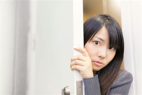 会議の様子をドアの隙間から覗く女性社員｜ぱくたそフリー素材