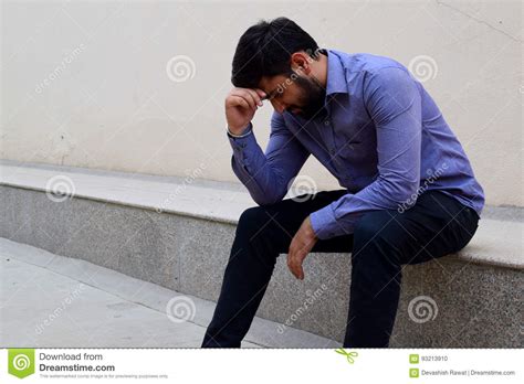 Stressed And Sad Young Man Sitting Outside Holding Head With A Hand