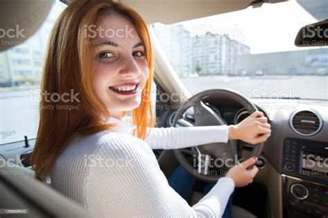 Young Redhead Woman Driver Behind A Wheel Driving A Car Smiling Happily