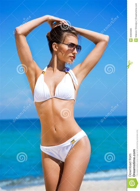 eine junge brunettefrau in einem weißen badeanzug auf dem strand stockbild bild von attraktiv