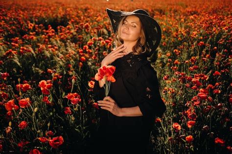 Una Chica Con Un Vestido Negro Y Un Sombrero En Un Campo De Amapolas Al Atardecer Foto Premium