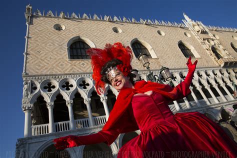 A Woman In A Red Dress And Headpiece Is Posing For The Camera With An Ornate Building Behind Her