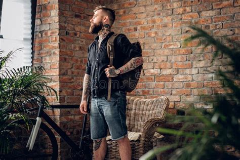 A Man With Tattoos On His Arms Holds Urban Backpack Stock Image