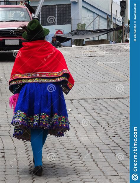 A Traditional Dressed Woman Of The Quechua Culture Walking Over A Paved
