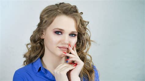 girl is blonde with curly hair in a bright blue shirt hands with bright red nails on the face