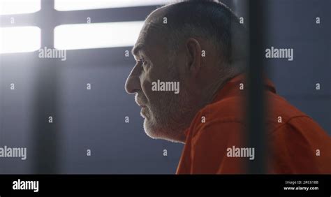 Elderly criminal in orange uniform sits on prison bed and dreams about