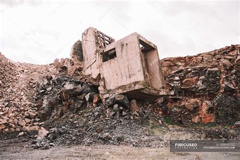 Piece Of Destroyed Cement Building On Open Pit With Rough Stones Under Cloudy Sky In Daylight