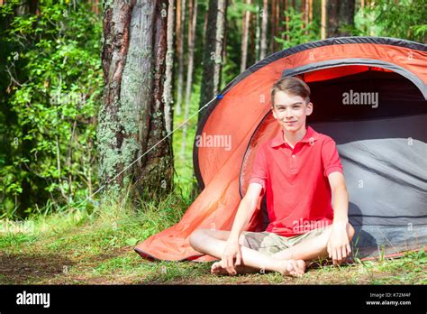Happy Teen Boy Sitting Barefoot By A Camping Tent In A Summer Forest