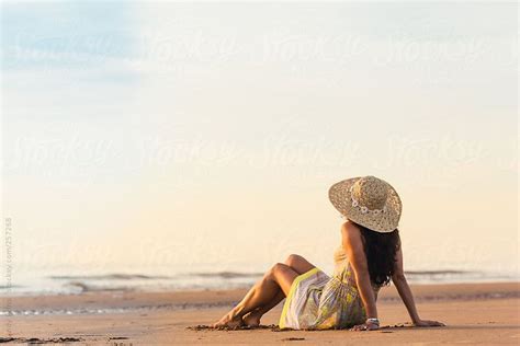woman in a dress with a sunhat on sitting on the beach by cindy prins beach photography poses
