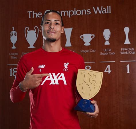 A Man Holding A Trophy And Plaque In Front Of A Wall With Trophies On It