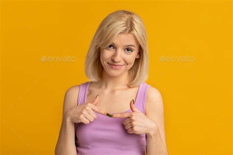 Shy Blonde Woman Joining Forefingers Together While Posing Over Yellow