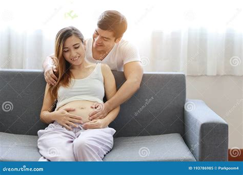 Medium Shot Of Young Caucasian Husband Embracing Young Asian Pregnant Belly Wife With Happiness