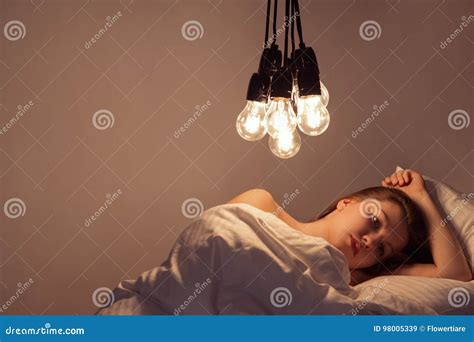 A Girl Lies In Bed Under Big Light Bulbs Can`t Fall Asleep Concept