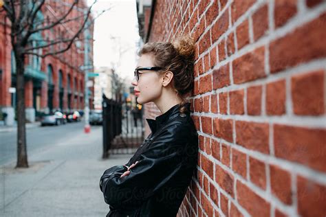 profile of a beautiful woman leaning against a brick wall in nyc by stocksy contributor