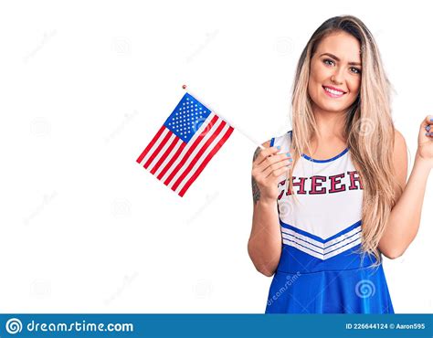 Young Beautiful Blonde Woman Wearing Cheerleader Uniform Holding United States Flag Smiling