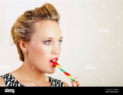 Portrait Of A Pretty Young Woman Biting Colorful Lollipop Stock Photo