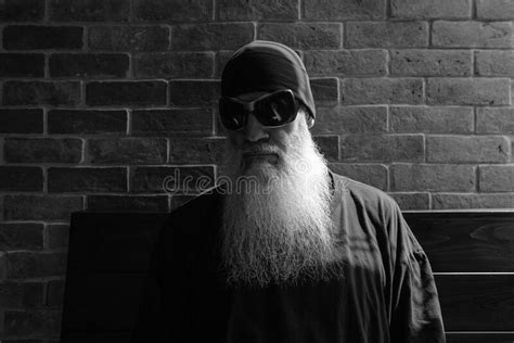 black and white portrait of mature man with long gray beard wearing beanie and sunglasses stock