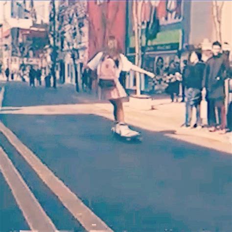 A Person Riding A Skateboard Down A Street Next To People Standing On