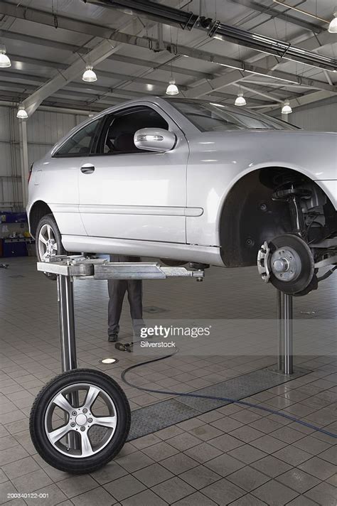 Mechanic Standing Behind Car Raised On Hydraulic Car Lift In Garage