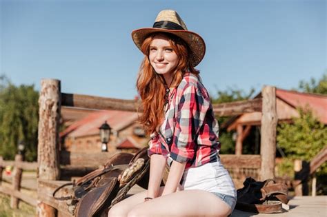 premium photo cheerful cute redhead cowgirl sitting and resting on the ranch fence