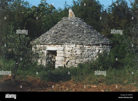 Round Stone House With Conical Roof Set Within And Partly Overgrown By