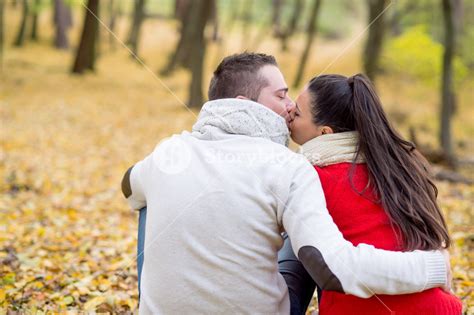 Beautiful Young Couple In Autumn Park Sitting On The Ground Covered