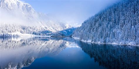 View Of Snowy Mountains Filled With Trees Next To A Calm Lake During