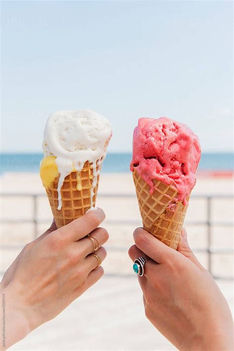 Two People Holding Ice Cream Cones In Their Hands On The Beach One Is