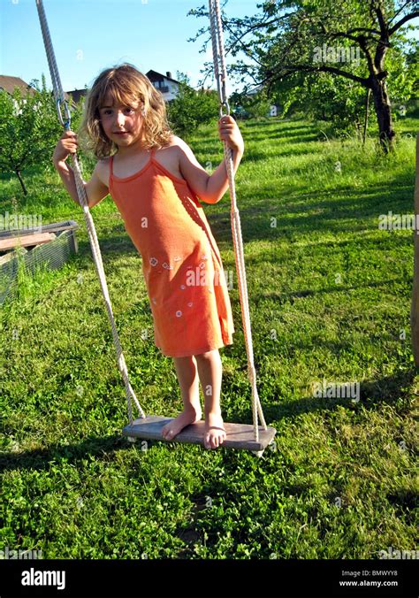 4 year old german girl in orange dress playing on an outdoor swing with a green pasture behind