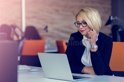 Attractive Charming Blonde Business Woman Talking On A Mobile While Sitting At Office Desk
