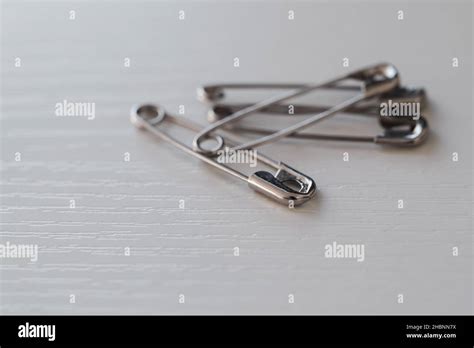 Closeup Of A Pile Of Four Metal Safety Pins On A White Desk Stock Photo