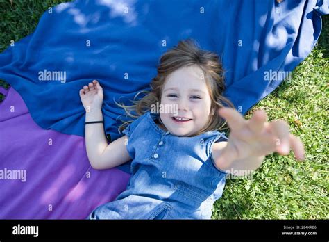 Four Years Old Blonde Girl Lying On Towels In The Green Grass Of Park