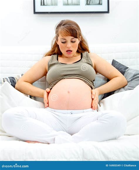 Überraschte holding der schwangeren frau ihr bauch auf sofa stockbild bild von getragen