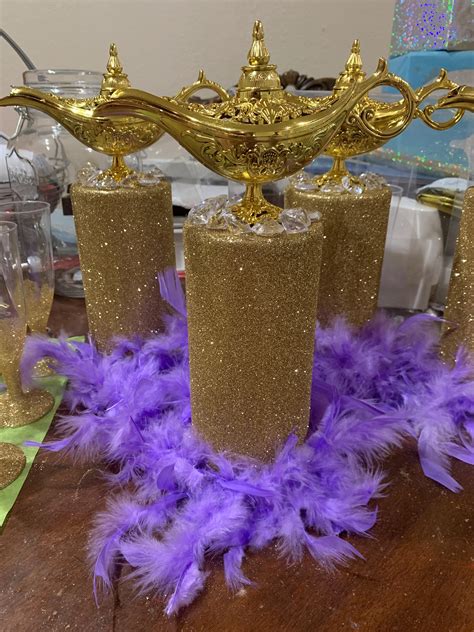 purple and gold feathers are on the table next to two vases with candles in them