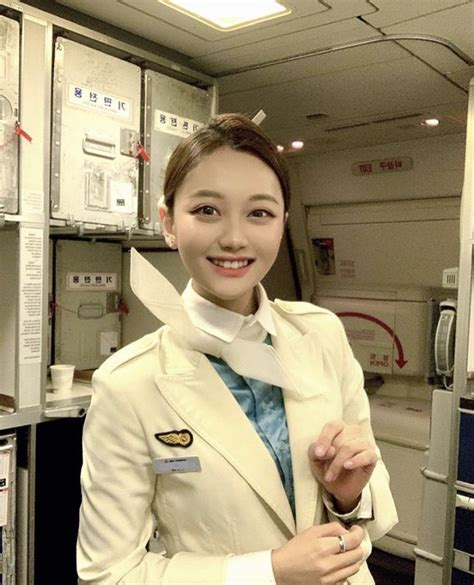 A Woman In An Airplane Cabin Wearing A White Suit And Blue Tie With Her Hands On Her Hips