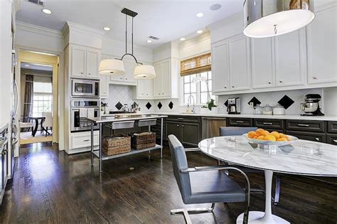 Beautifully appointed blue and white kitchen boasts navy blue cabinets fitted with polished nickel hardware and a white quartz countertop positioned beneath white folding windows and wrapping around to a stainless steel oven range placed against white beveled subway backsplash tiles beneath white upper cabinets. White Upper Cabinets Black Lower Cabinets - Contemporary - Kitchen