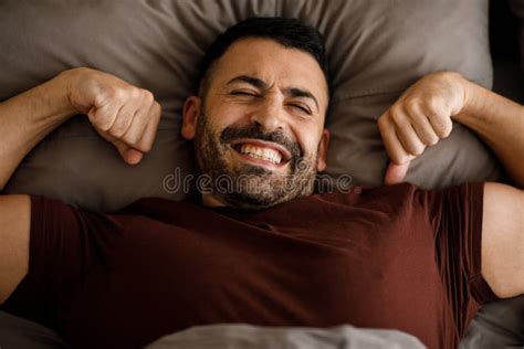 A Well Rested Guy In Burgundy Pajamas Wakes Up With His Arms Outstretched While Lying In Bed At