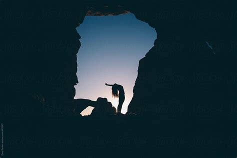 A Woman Stretching Beneath A Rock Arch Cave On Sunrise By Stocksy