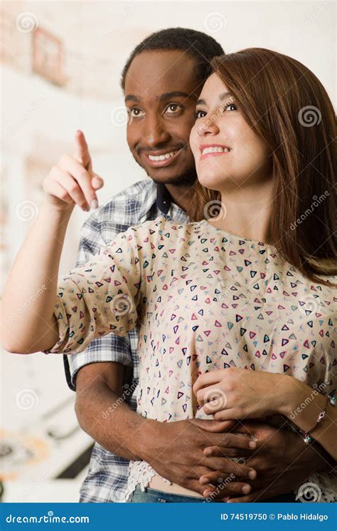 Happy Interracial Couple Embracing And Posing Happily Man Holding Around Woman From Behind