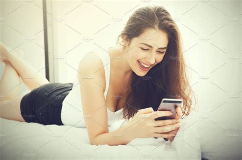 Beautiful Caucasian Woman Laying Down On White Bed Using Mobile Phone