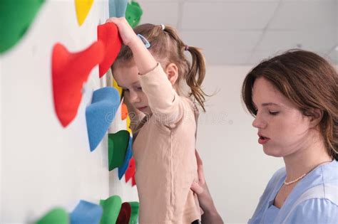Physiotherapist Instructor Helping Little Girl To Climb Wall In Gym