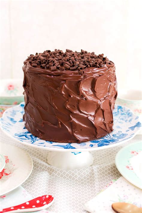 A Chocolate Cake Sitting On Top Of A White Plate Next To Plates And Spoons